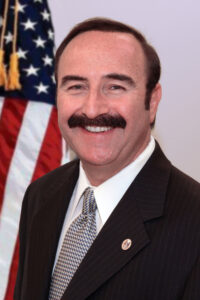 Man with a mustache smiling in front of an American flag